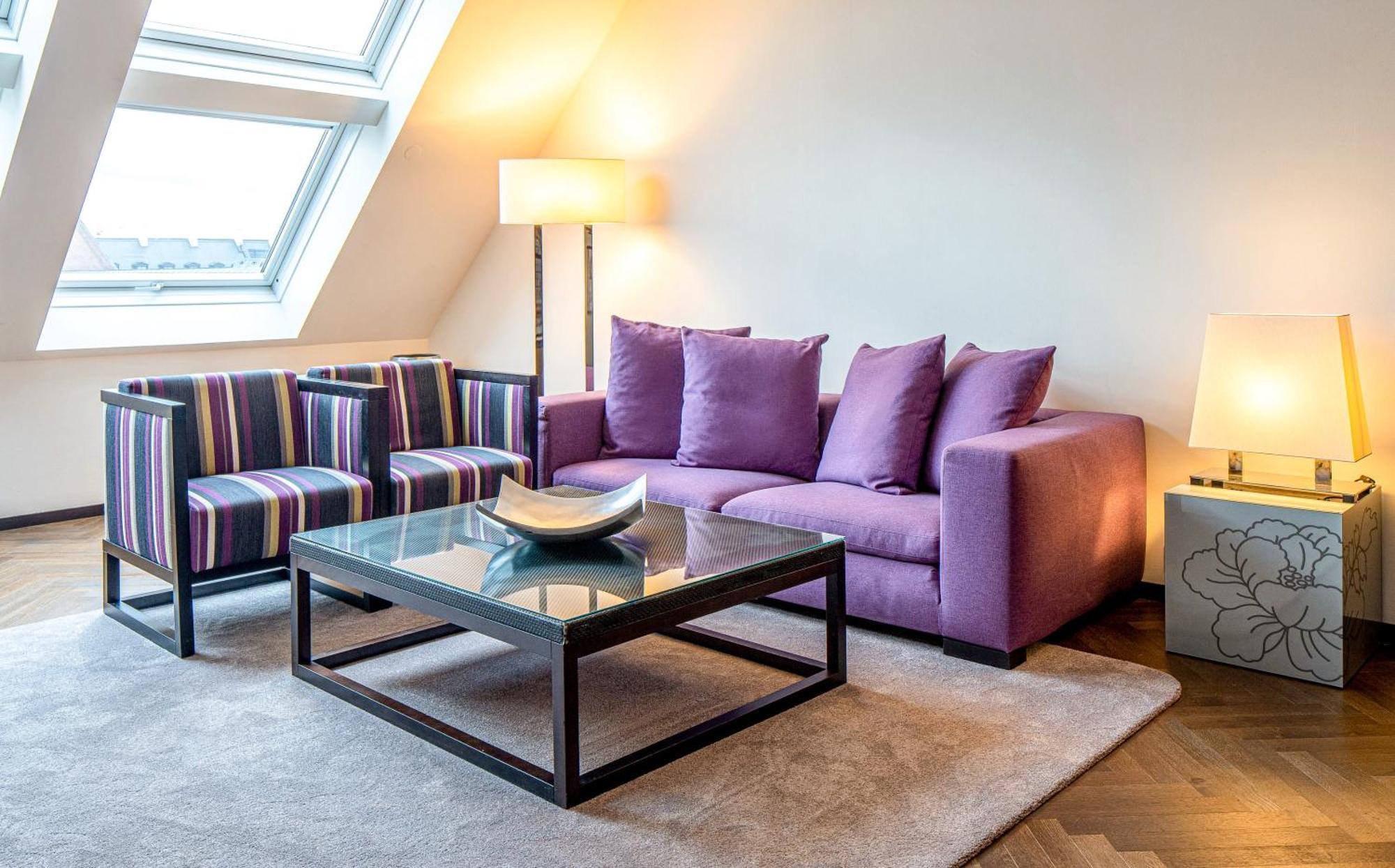 Steigenberger Hotel Herrenhof Wina Bagian luar foto The photo shows a modern living room setting. In the center, there is a stylish glass coffee table with a decorative bowl on it. Surrounding the table, there is a light beige carpet on the floor. 

On the left, there are two striped armchairs featuri